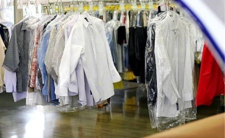 Several collared shirts and garments covered in plastic hang on racks at a dry cleaning shop.